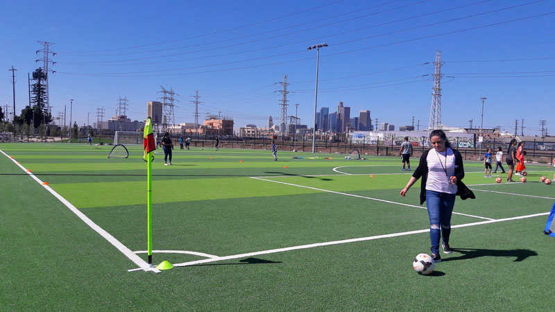 After construction, a woman follows a soccer ball on a green turf soccer field