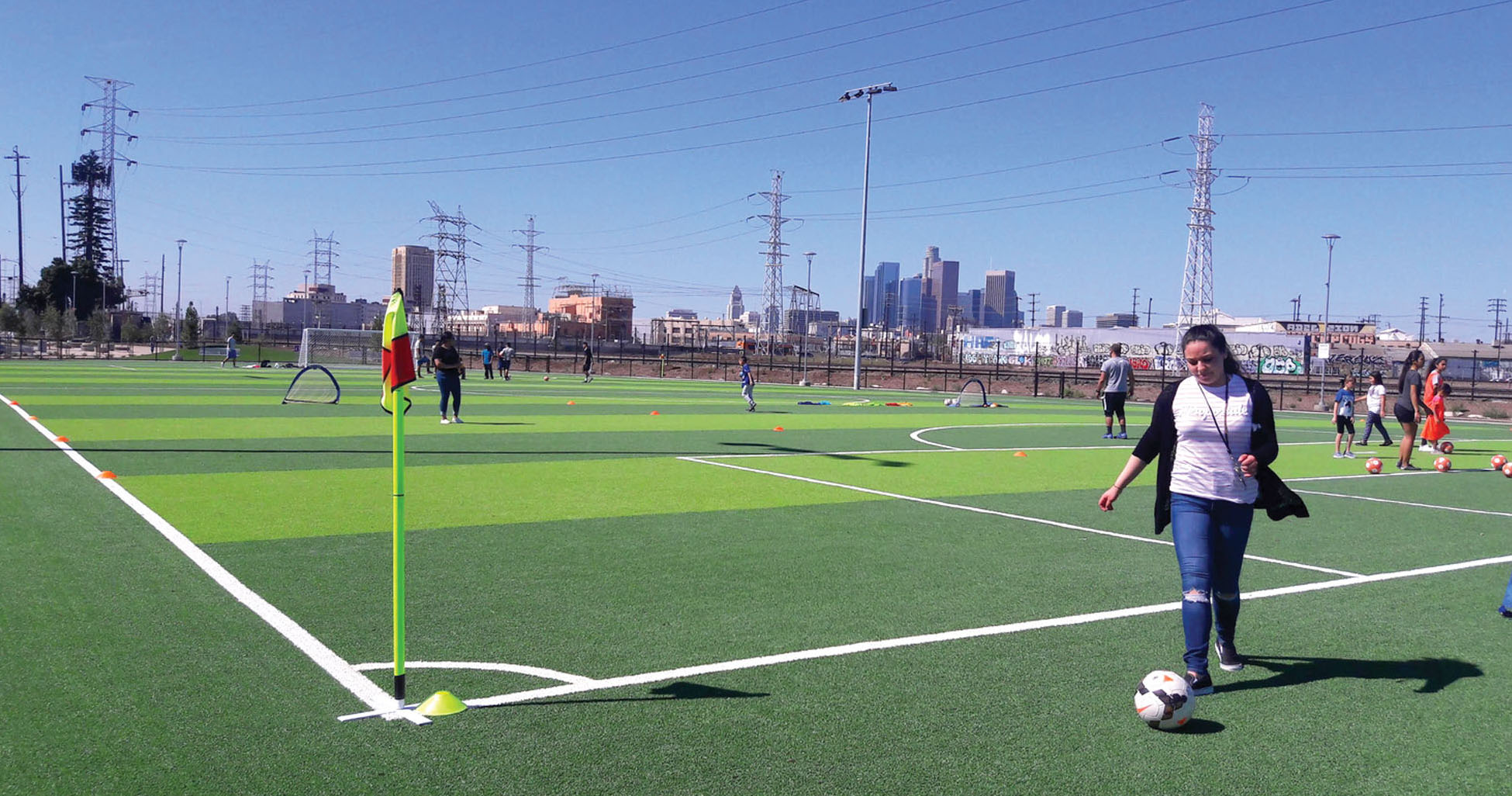 People practicing soccer on a new turf field with power lines in the background