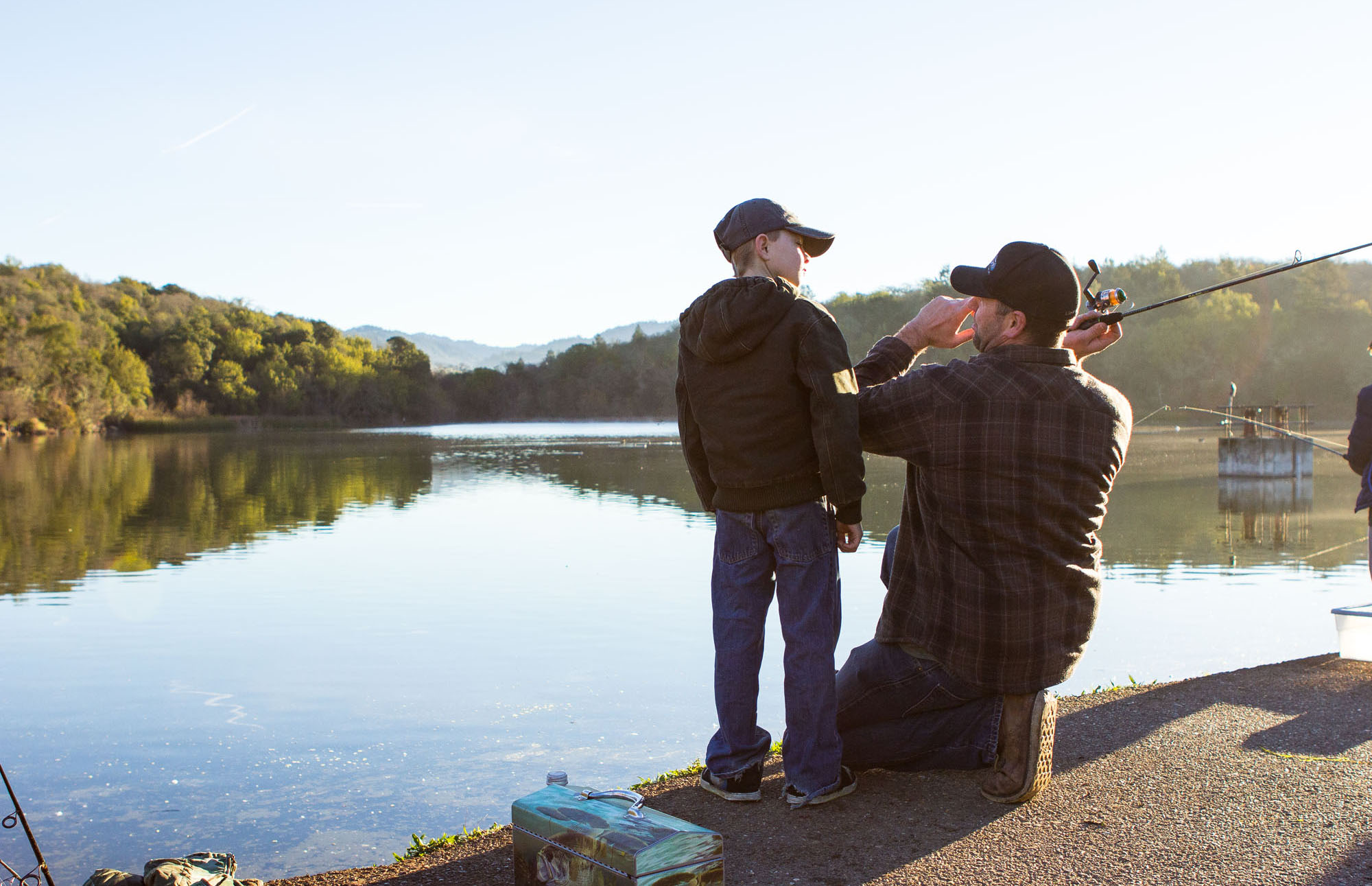 A father teaches his son how to cast a fishing rod and reel into a lake